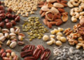 A variety of healthy and organic nuts and seeds in piles on a slate surface.